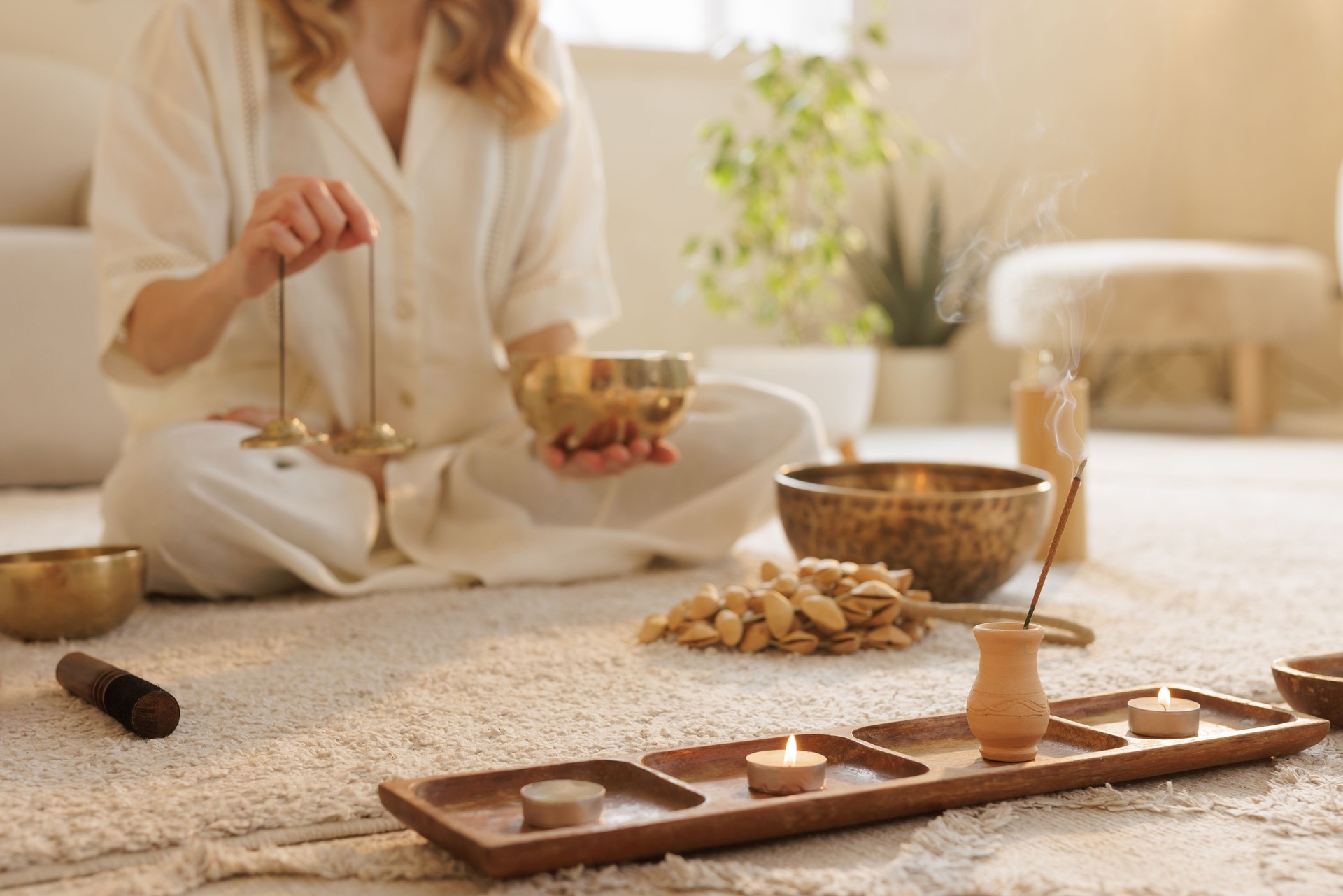 Woman in meditation using singing bowls, incense, and candles in a peaceful wellness setting.