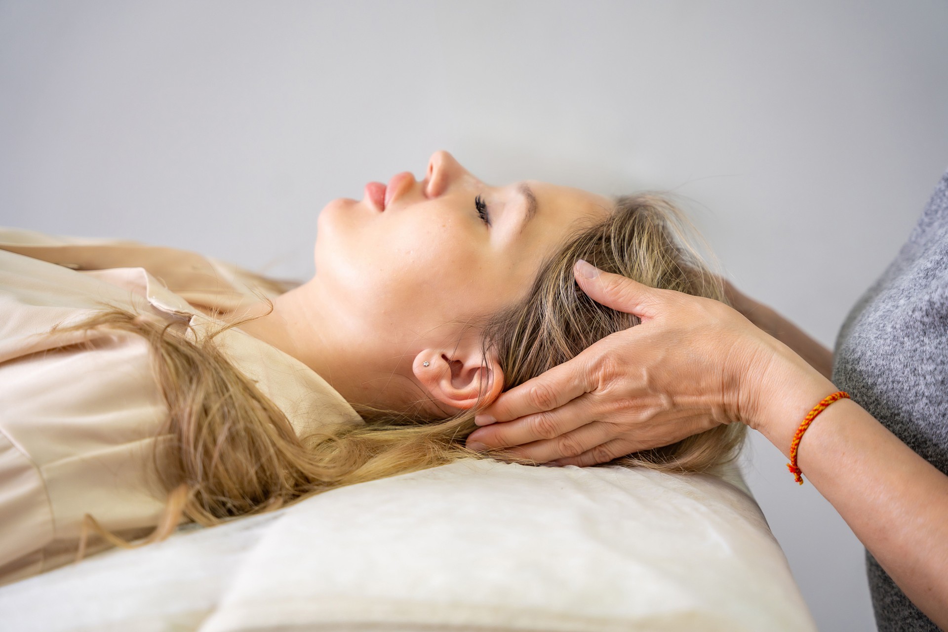 Female practitioner performs facial lifting technique on a young woman lying on a couch. Concept of energy healing, face therapy and alternative wellness practice from Access Bars.